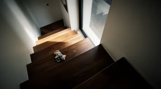 Vue cinématographique d'un escalier intérieur en bois avec rampe métallique, éclairage dramatique créant des ombres profondes