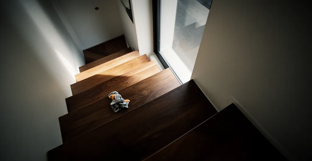 Vue cinématographique d'un escalier intérieur en bois avec rampe métallique, éclairage dramatique créant des ombres profondes