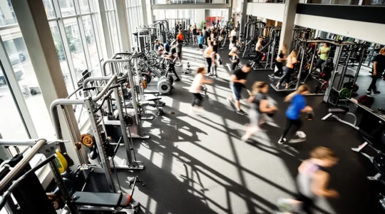 Vue aérienne d'une salle de sport moderne avec des équipements variés et des personnes en pleine activité physique, juxtaposée à des documents administratifs flous en arrière-plan