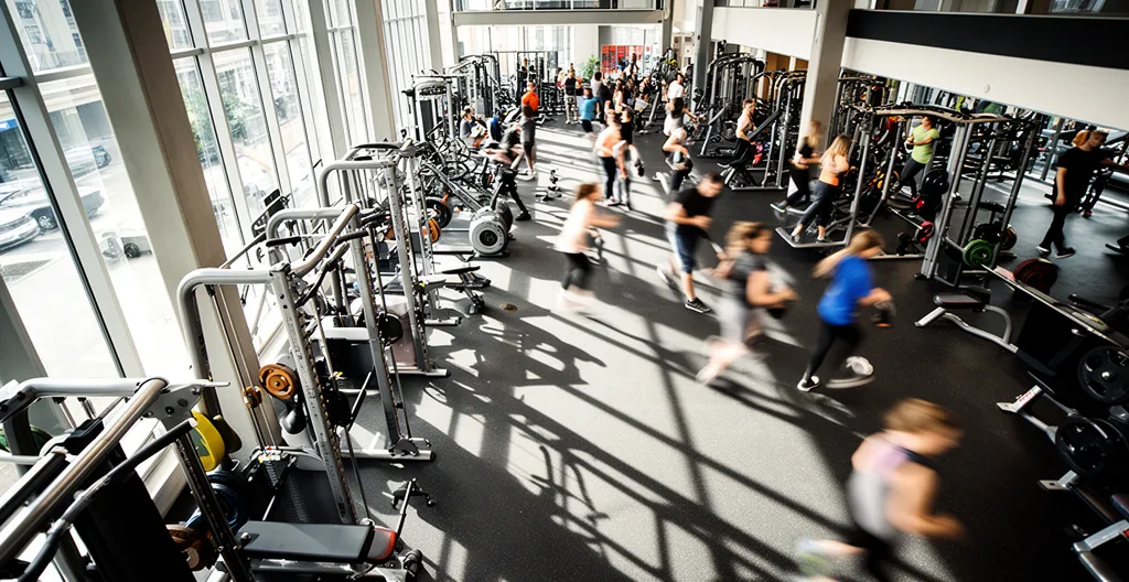 Vue aérienne d'une salle de sport moderne avec des équipements variés et des personnes en pleine activité physique, juxtaposée à des documents administratifs flous en arrière-plan